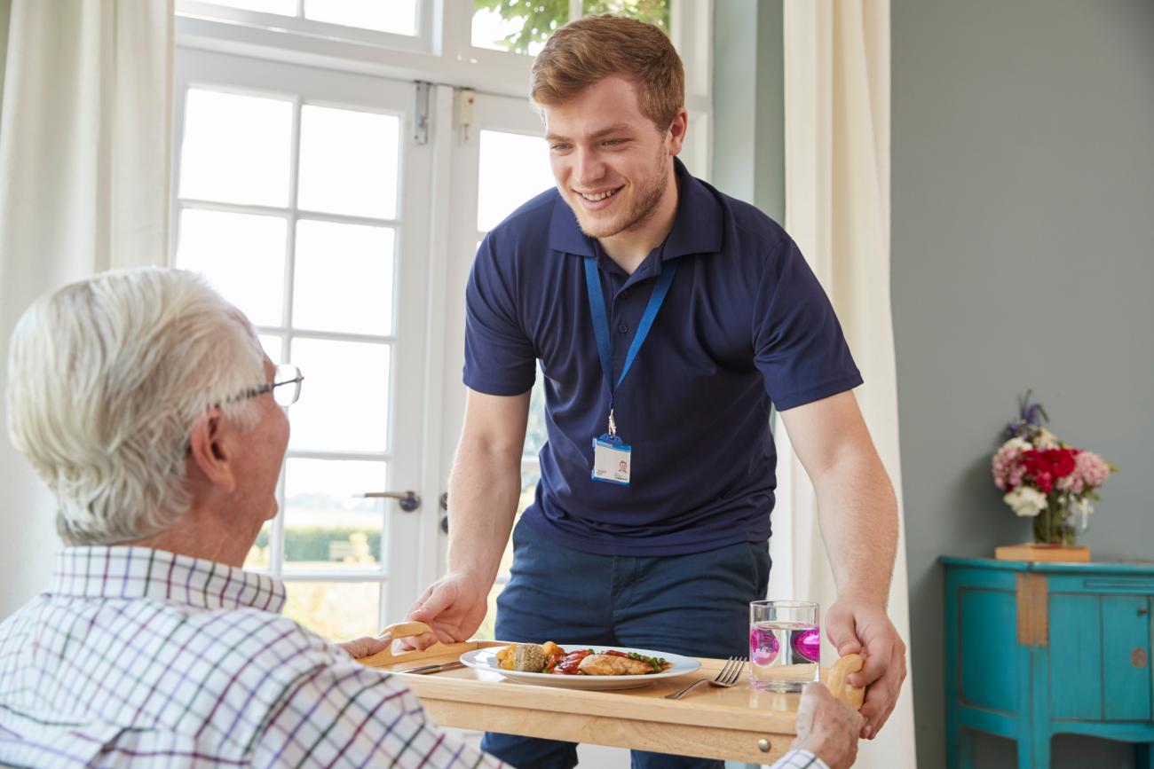 a nursing assistant brings food to a older man