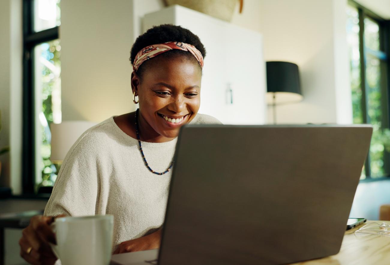 Smiling woman sitting at a table on her laptop reading the Caregiving in Action newsletter.
