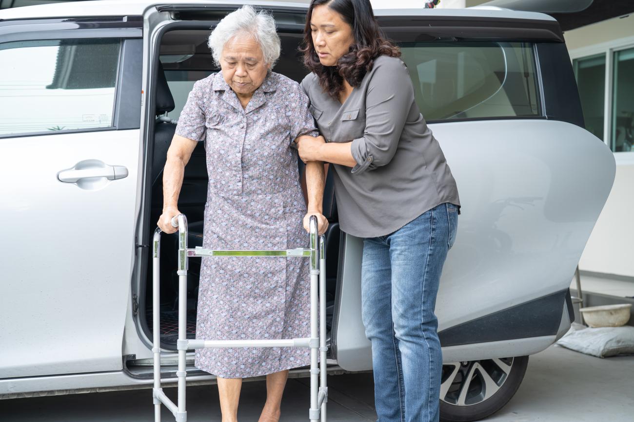 Caregiver helping elderly parent out of the van.