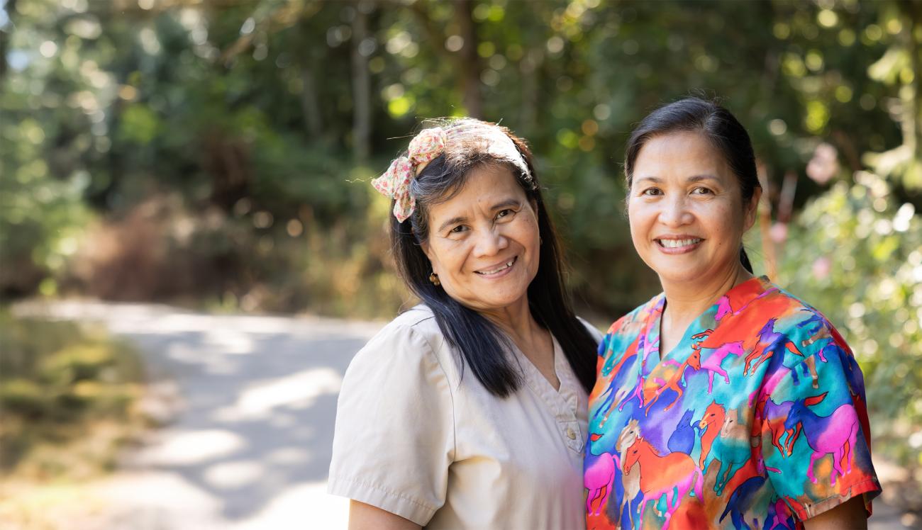 Two smiling paid caregivers standing together outside.