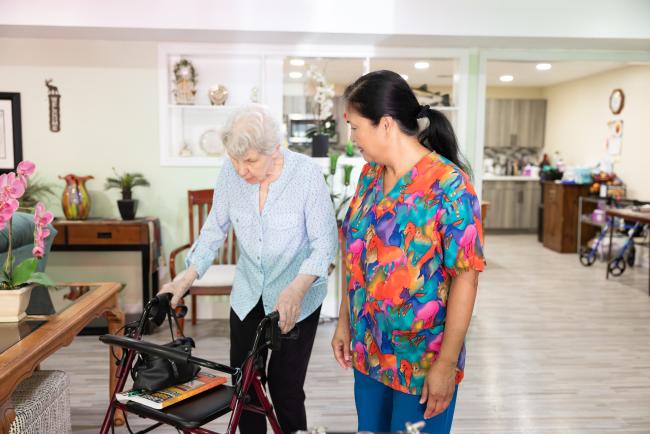 Caregiver helping a client walk while using a walker.